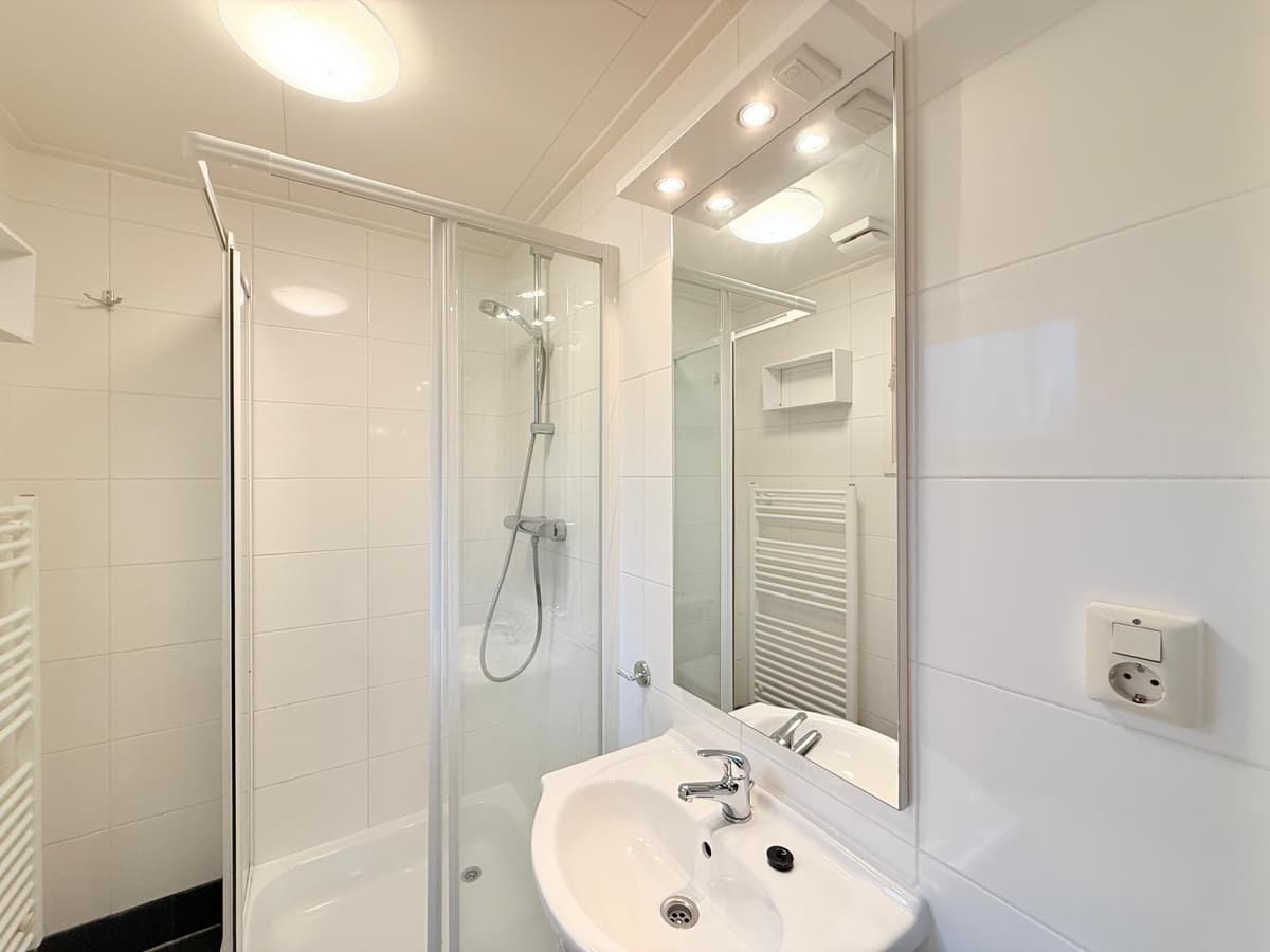 Moderne badkamer met douchecabine, wastafel en spiegel, witte tegels en handdoekradiator.