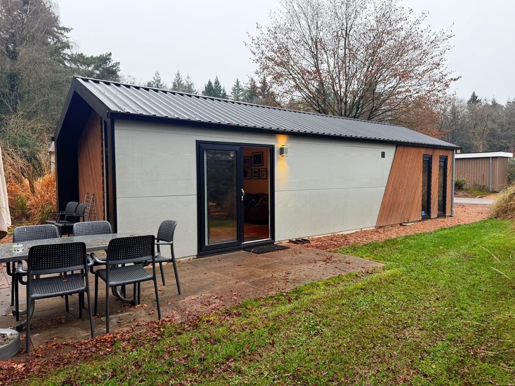Moderne vakantiewoning met een combinatie van houten en gladde gevel, uitzicht op groene tuin met terrassen en meubels.