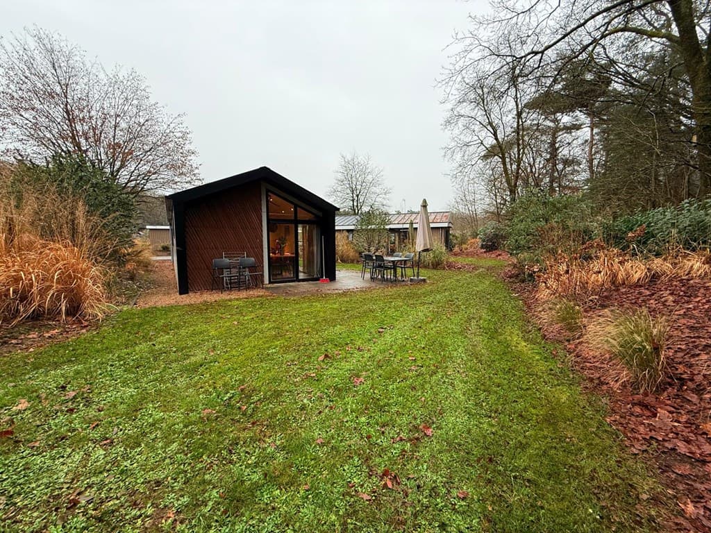 Moderne vakantiewoning met grote tuin en zitplaatsen, omringd door bomen en gras op EuroParcs Resort De Utrechtse Heuvelrug.