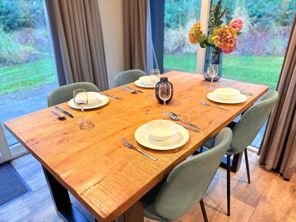 Eettafel met vier stoelen, gedekte tafel met servies en uitzicht op de tuin door grote raampartij