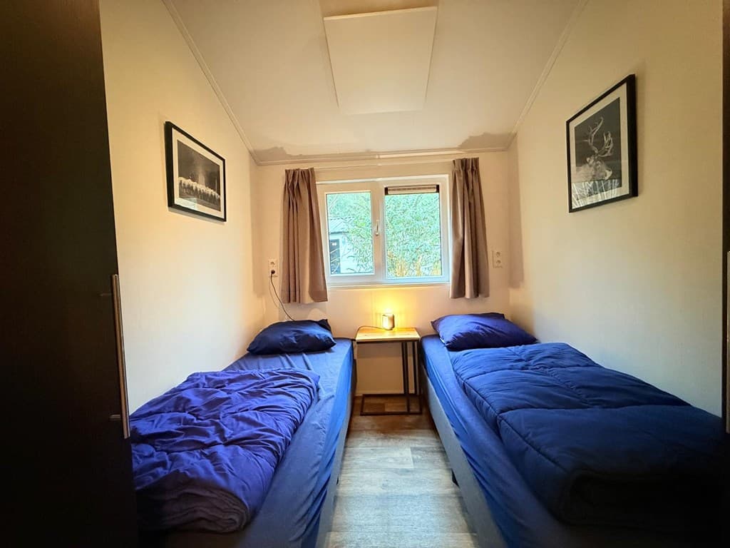 Slaapkamer met twee eenpersoonsbedden, raam met gordijnen en een nachtkastje tussen de bedden.