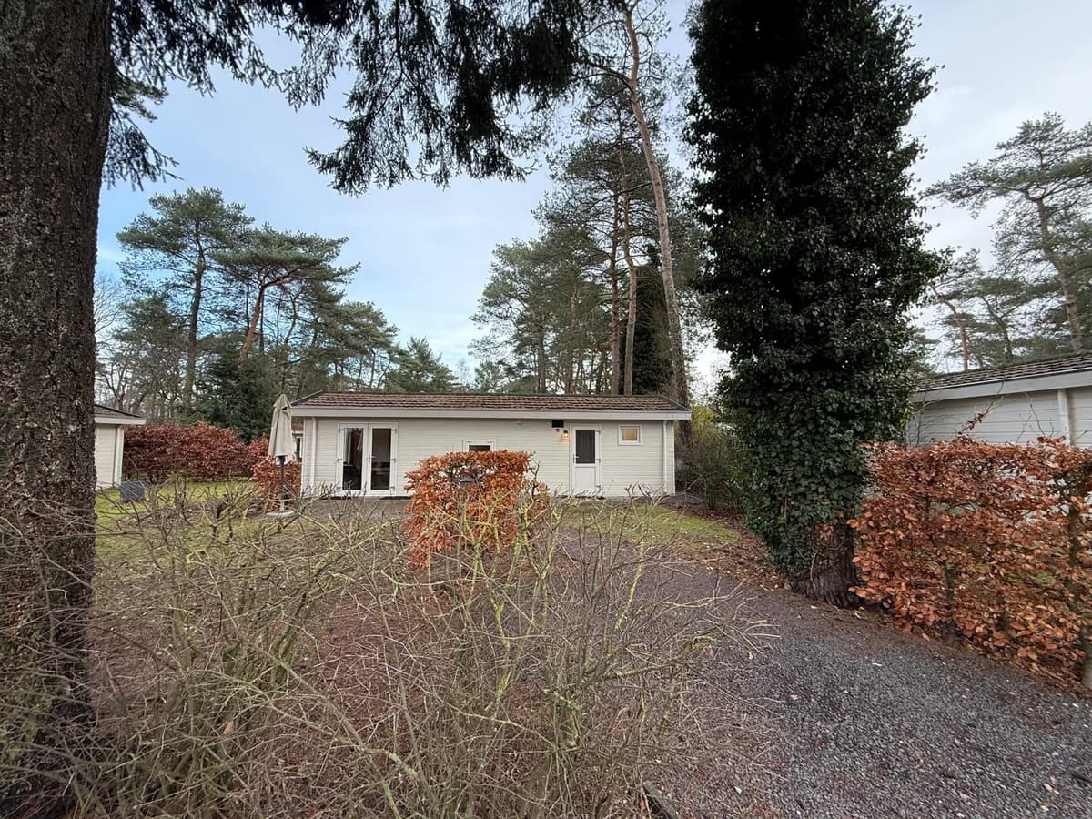 Vakantiewoning omringd door bomen en hagen, met een oprit en glazen deuren aan de voorkant.