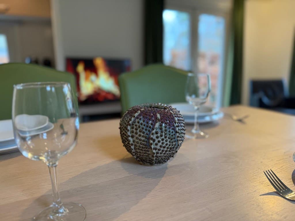 Eettafel met glazen en een decoratief object, op de achtergrond een openhaard met vlammen in een woning