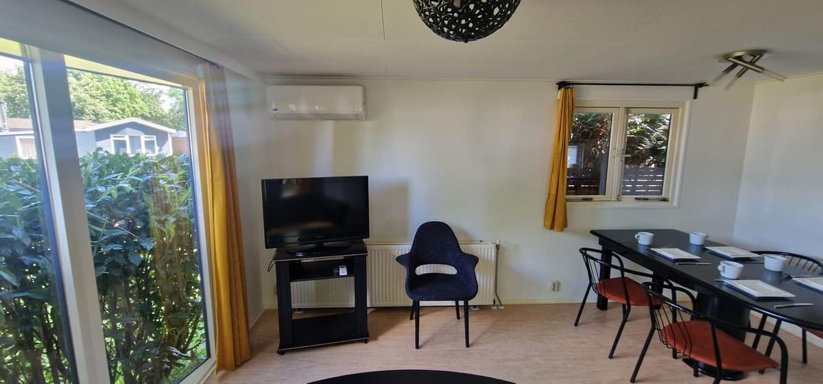 Modern interieur met zitgedeelte, televisie en eettafel bij raam met uitzicht op de buitenruimte.
