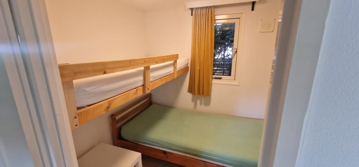 Slaapkamer met een stapelbed, een éénpersoonsbed en een raam met uitzicht op de buitenruimte.
