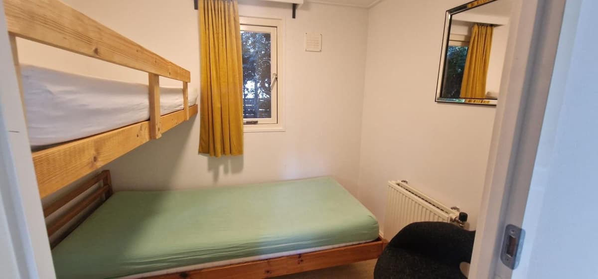 Slaapkamer met stapelbed, een eenpersoonsbed, een raam met gordijnen en een wandspiegel.