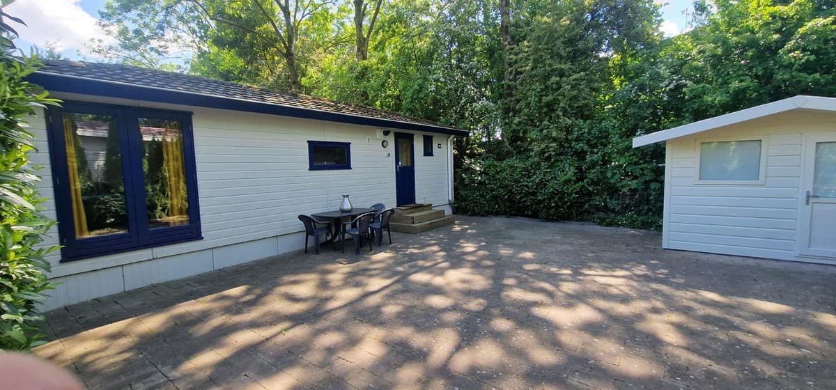 Uitzicht op een vakantiewoning met een terras en een tuinhuisje, omringd door bomen en groen.