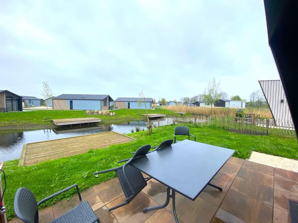 Buitenterras met een tafel en stoelen, uitzicht op een vijver en vakantiewoningen in de omgeving