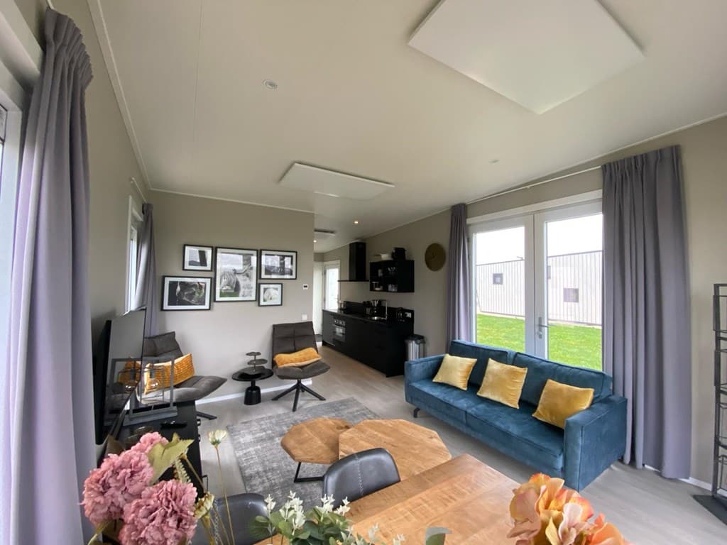 Lichte woonkamer met moderne meubels, grote ramen en toegang tot de buitenruimte, groene tuin op achtergrond.