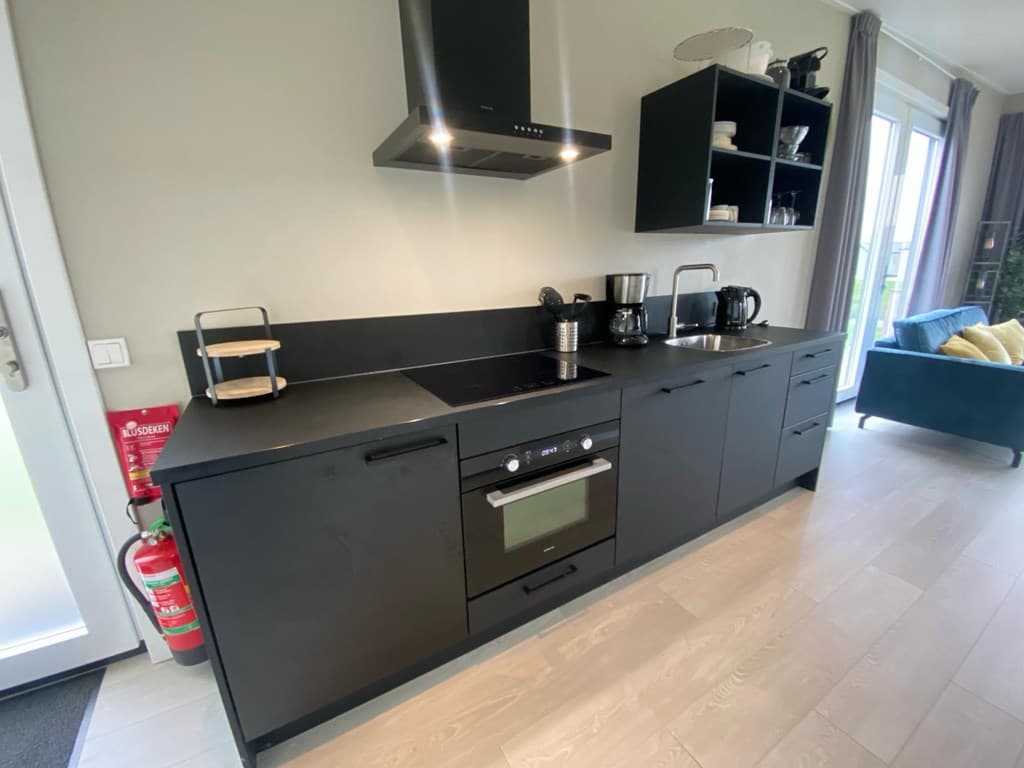 Moderne zwarte keuken met ingebouwde apparatuur, koffiezetapparaat en uitzicht op de woonkamer.