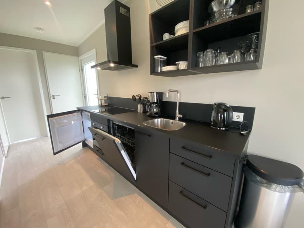 Zwarte keuken met inbouwapparatuur, voorraadkasten en open planken met glazen servies en kookaccessoires.