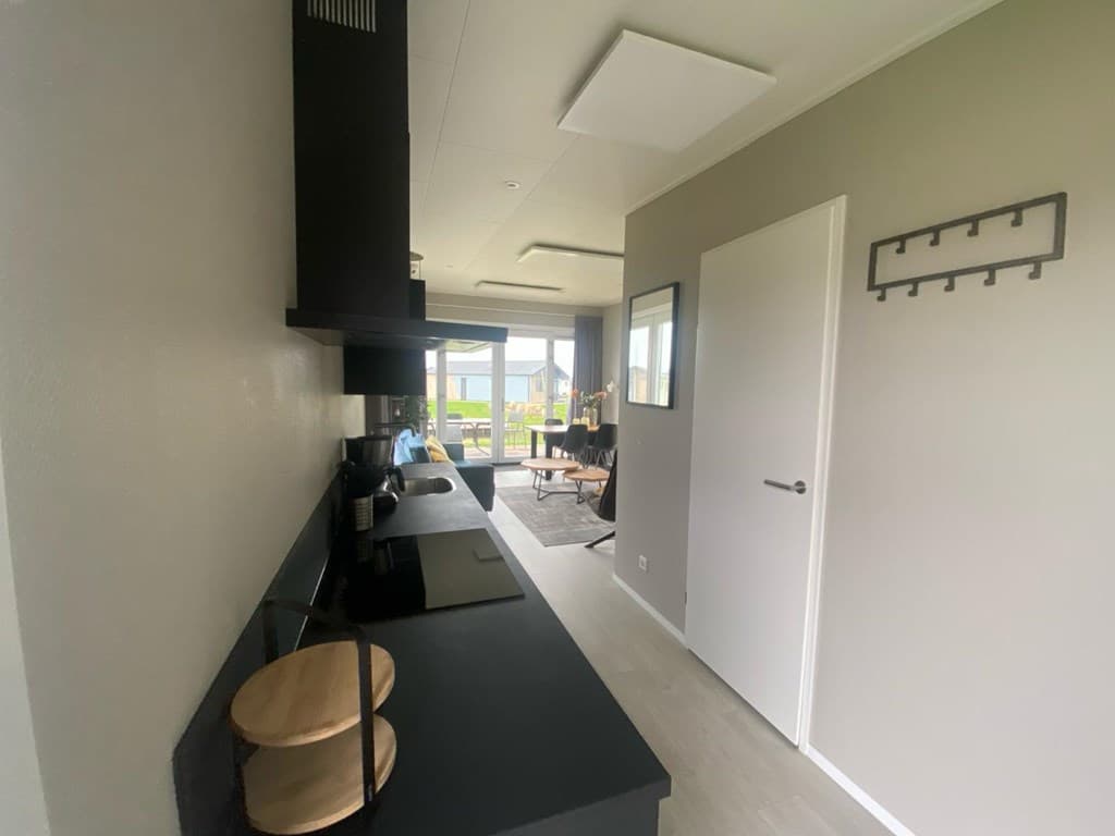 Moderne keuken met zwart werkblad en open verbinding naar de woonkamer met uitzicht op het terras en de tuin.