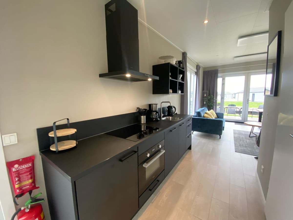 Moderne keuken met zwarte kasten, apparatuur en een eettafel in een lichte woonruimte met toegang tot de tuin.