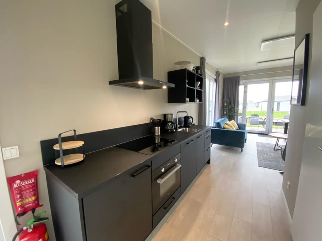 Moderne keuken met zwarte kasten, apparatuur en een eettafel in een lichte woonruimte met toegang tot de tuin.