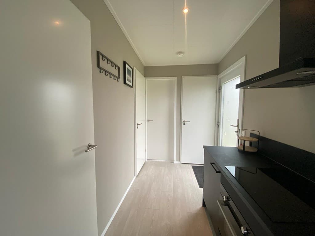 Ingang van de woning met een lange gang, lichte muren, en zwarte keukeninrichting aan de rechterzijde.