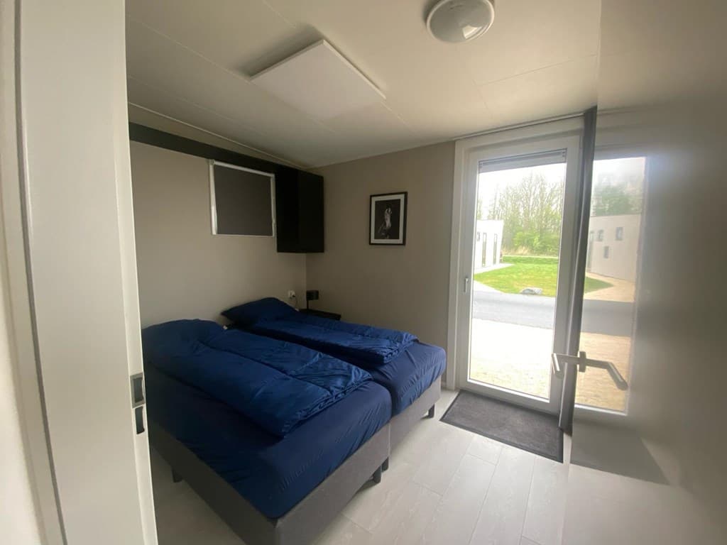Slaapkamer met twee losse bedden, grote ramen en lichtgrijze muren.