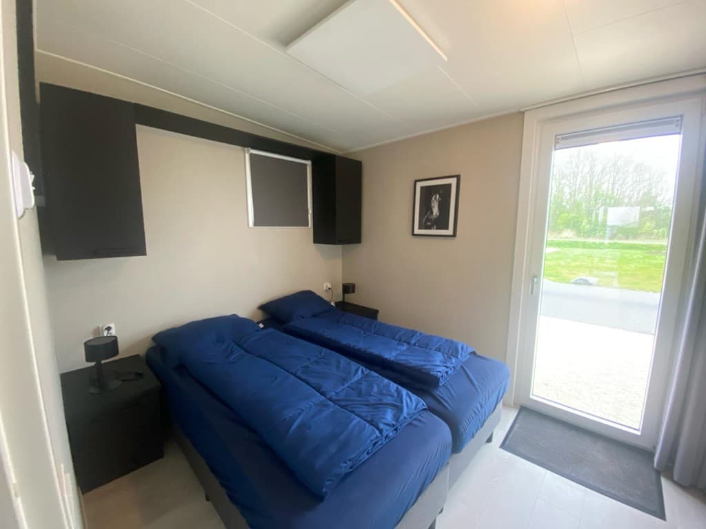 Slaapkamer met twee losse bedden, kastjes, lampen en openslaande deuren naar buiten met uitzicht op gras.