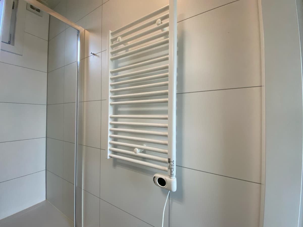 Witte handdoekradiator aan de wand in een moderne, betegelde badkamer met douche.