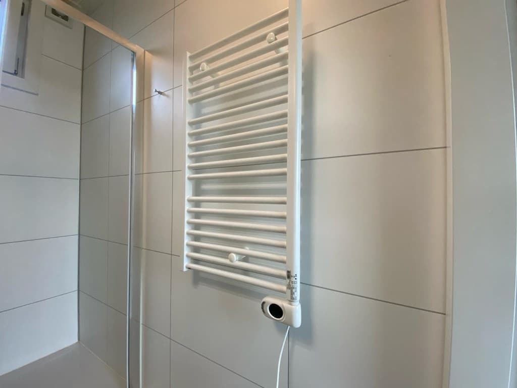 Witte handdoekradiator aan de wand in een moderne, betegelde badkamer met douche.