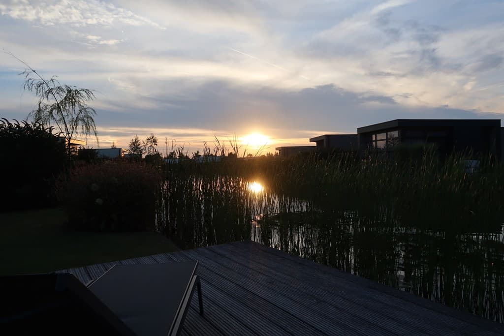 Zonsondergang boven het water met riet, omringd door moderne woningen en groene planten.