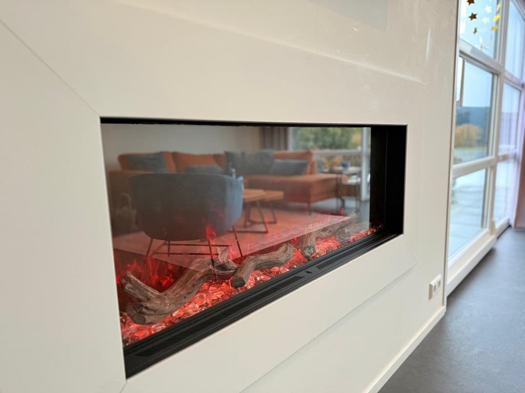 Modern elektrische haard met zicht op een zithoek met een bank en vloerkleed in de achtergrond.