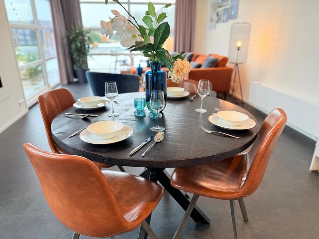 Eettafel met vier leren stoelen, gedekte tafel en een decoratie met bloemen en vazen in een moderne leefruimte.