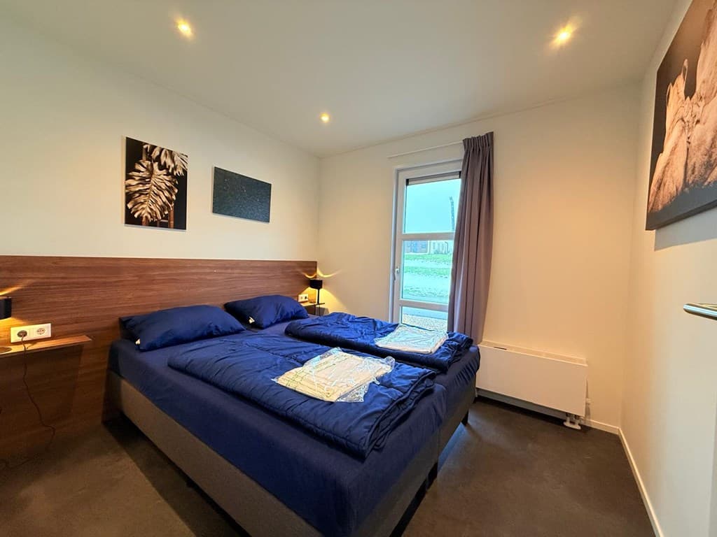 Slaapkamer met twee eenpersoonsbedden, nachtkastjes en toegang tot buiten via een deur met een raam.