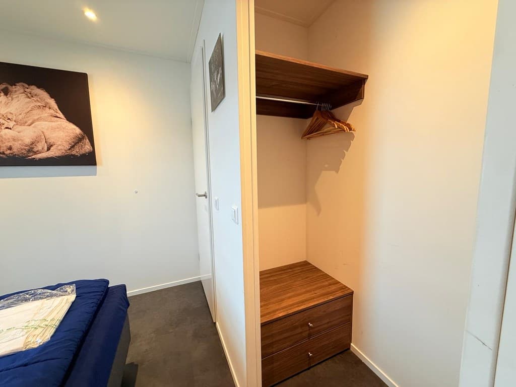 Ingerichte kastenwand met hangruimte en lade in een lichte slaapkamer met een schilderij aan de muur.