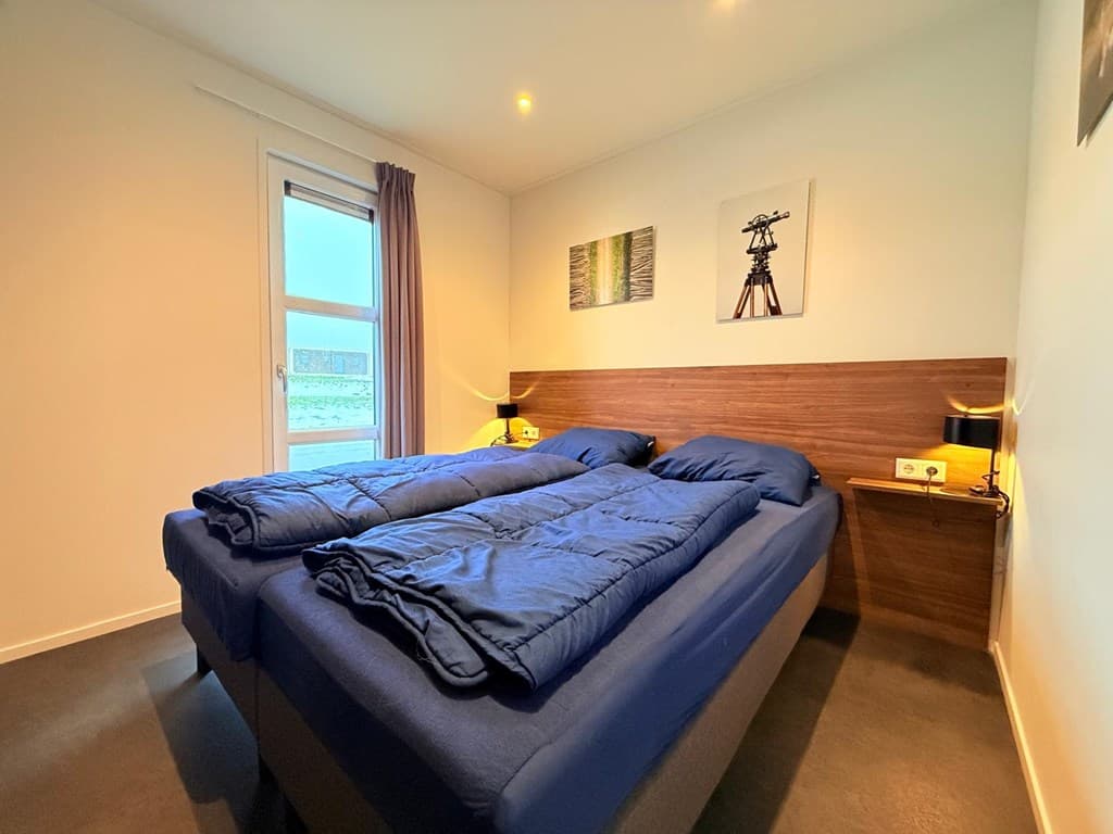 Slaapkamer met twee aparte bedden, houten wand, nachtlampjes en een raam met uitzicht naar buiten