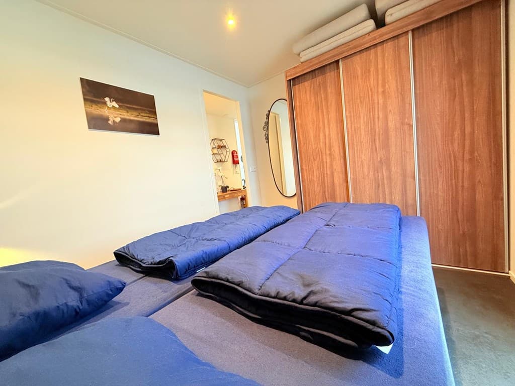 Slaapkamer met twee eenpersoonsbedden, kledingkast en deur naar de badkamer in een vakantiewoning