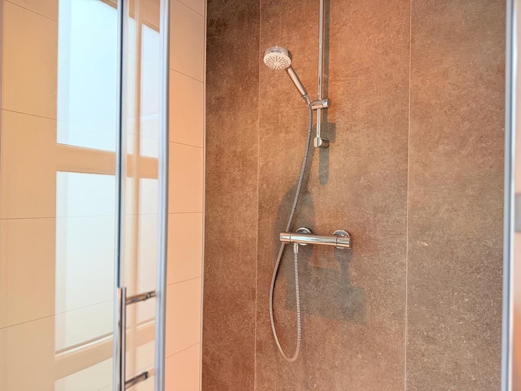 Moderne douche met glazen deur en wandtegels in een neutrale kleurstelling.
