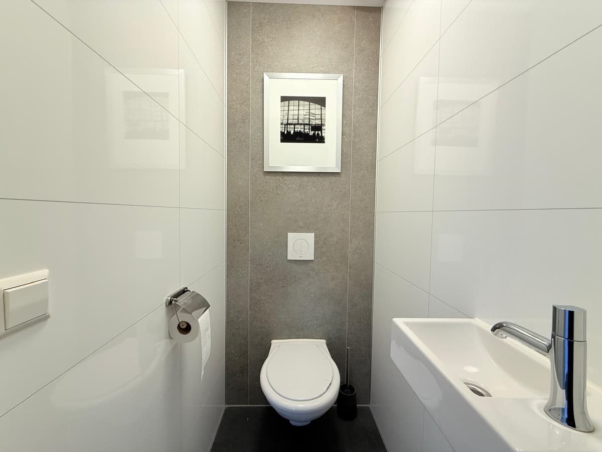 Luxe, moderne wc met een wandcloset, fonteintje en kunst aan de muur in een strakke, lichte ruimte