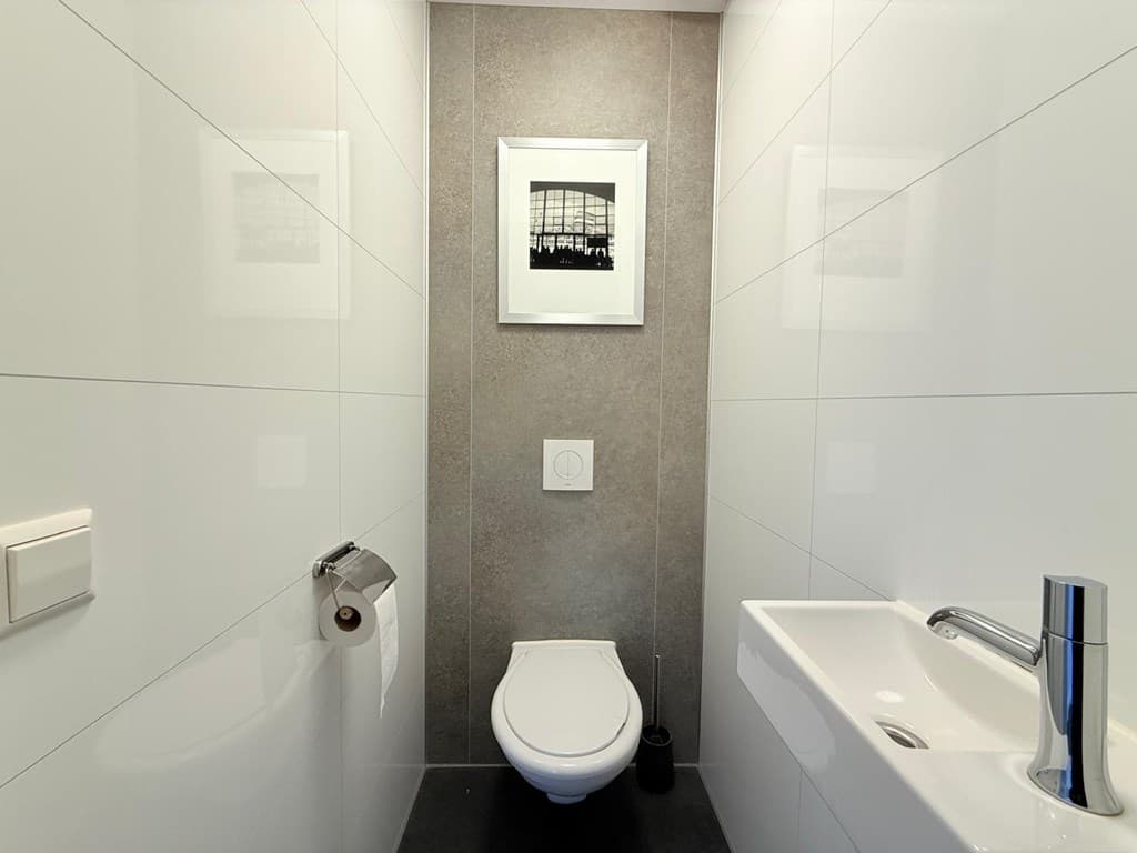 Luxe, moderne wc met een wandcloset, fonteintje en kunst aan de muur in een strakke, lichte ruimte