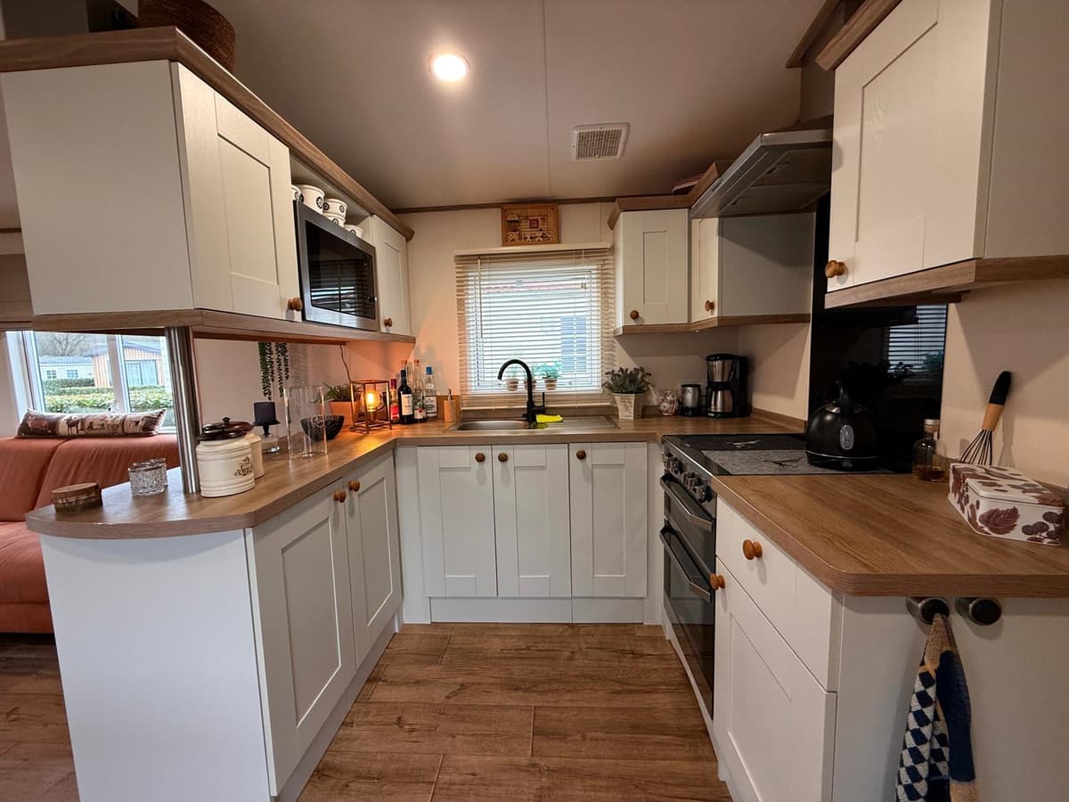 Keuken met lichte kastjes, houten aanrecht en moderne apparatuur, uitzicht op de woonkamer met een bankstel