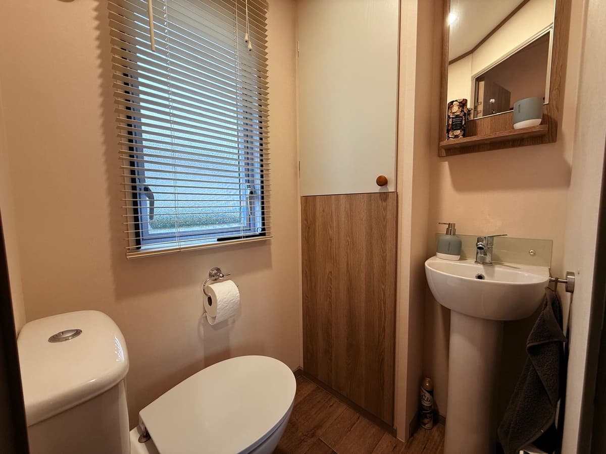 Toilet met wastafel en spiegel, gordijnen voor het raam en houten accenten aan de muur