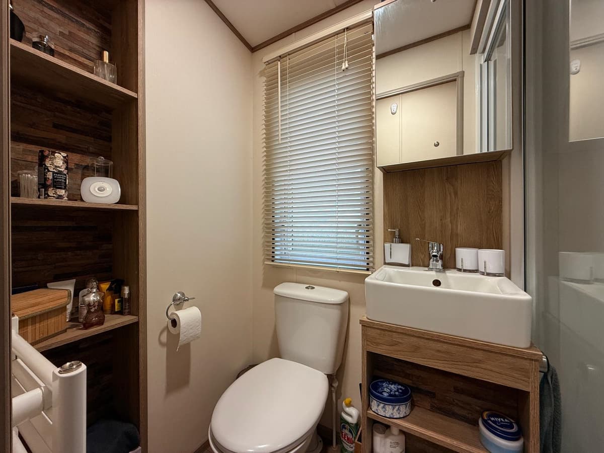 Witte wc met wastafel en kastje in een lichte badkamer met houten accenten en houten planken aan de muur
