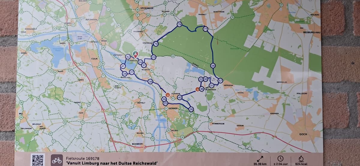 Kaart met fietsroutes van Limburg naar het Duitse Reichswald, weergegeven op een bakstenen muur met informatie over afstand e