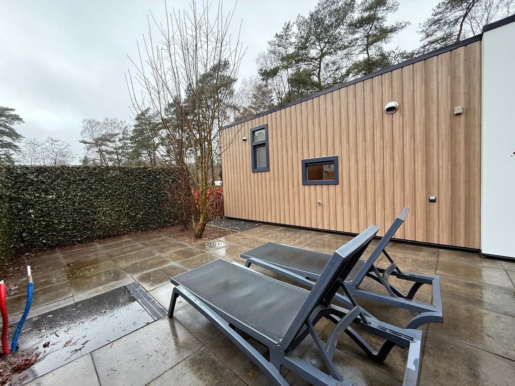Terras met twee ligstoelen en moderne houten wand, omringd door groene hagen en met een betegelde vloer