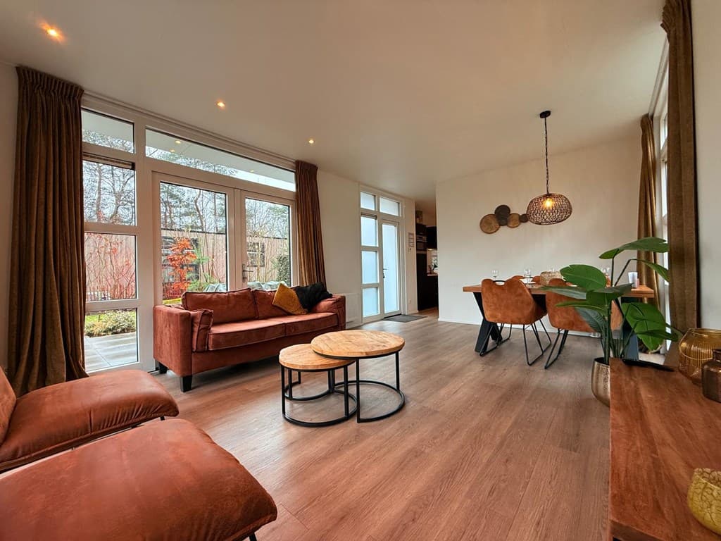 Woonkamer met een zithoek, eettafel en grote ramen met uitzicht op de tuin