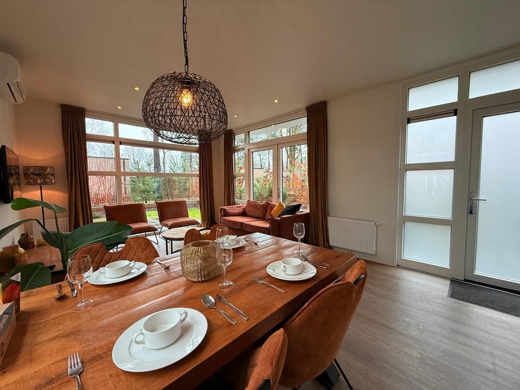 Eetkamer met een houten tafel en stoelen, zithoek met bank, grote ramen en toegang naar buiten