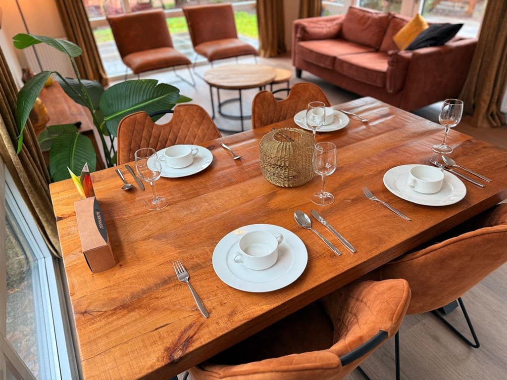 Eetkamer met een houten tafel, vier leren stoelen en een gezellige zithoek met een bank en grote ramen.