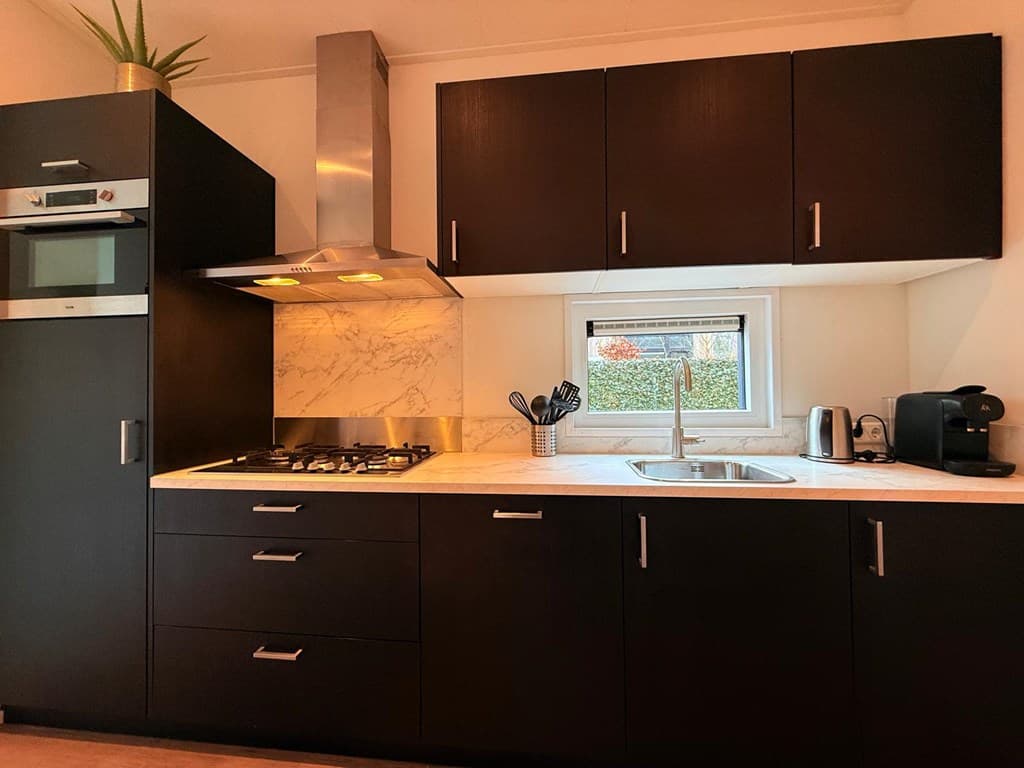 Moderne keuken met donkere kasten, een marmeren werkblad en een raam met uitzicht naar buiten.