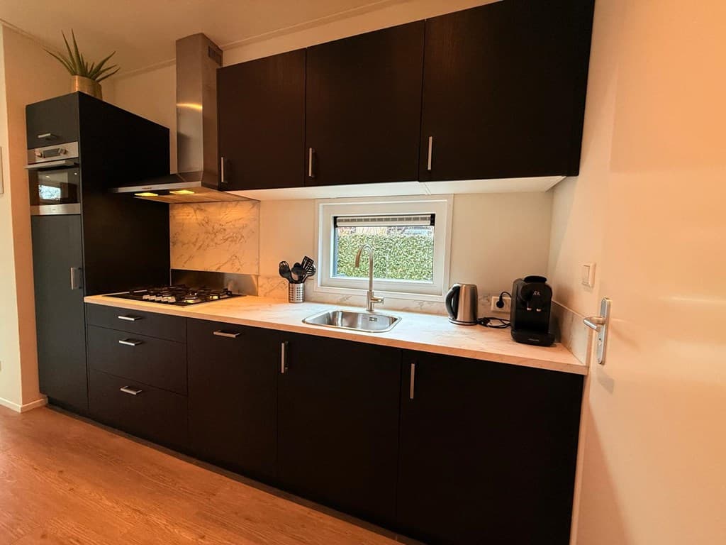 Moderne keuken met zwarte kasten, marmeren aanrecht, een gootsteen en keukenapparatuur zoals een koffiezetapparaat.