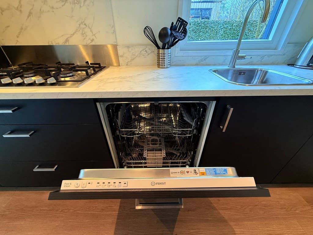 Keuken met zwarte kastjes, een spoelbak bij het raam, een afwasmachine en een gaskookplaat op een marmeren aanrechtblad