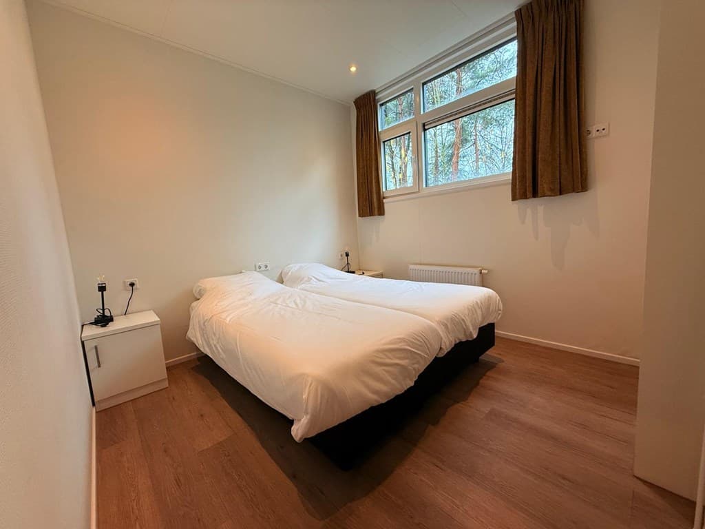 Slaapkamer met twee eenpersoonsbedden, nachtkastje en lichtinval vanuit grote ramen.