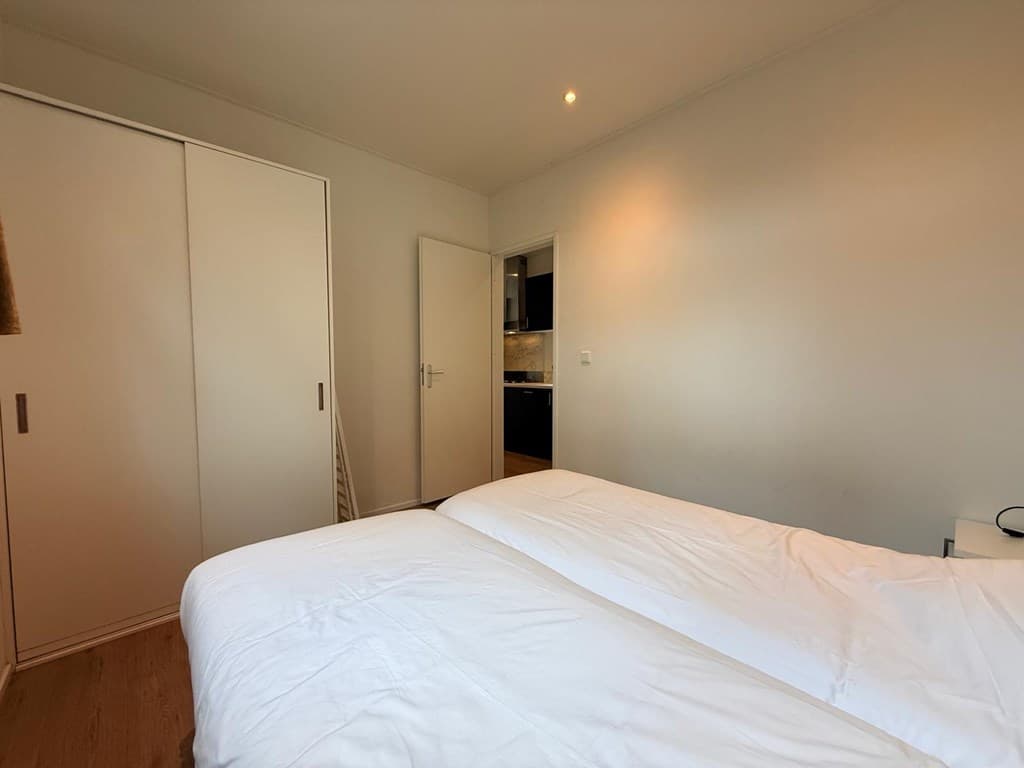 Slaapkamer met twee eenpersoonsbedden en een kast, toegang tot de keuken zichtbaar in de achtergrond.