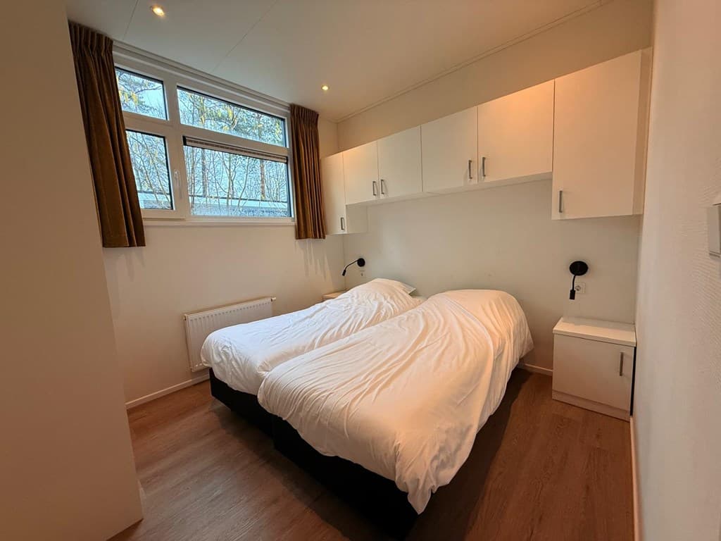 Sfeervolle slaapkamer met twee eenpersoonsbedden, wandkasten en raam met uitzicht op groen.