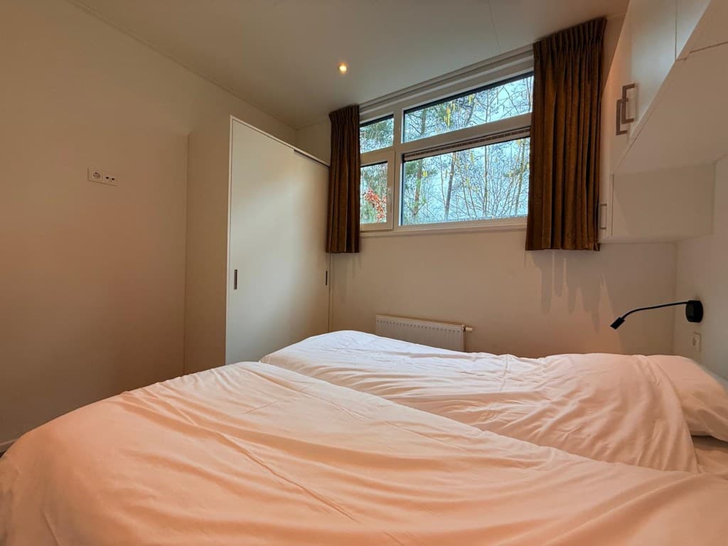 Slaapkamer met twee eenpersoonsbedden, ramen met uitzicht op bos en een kast tegen de muur.