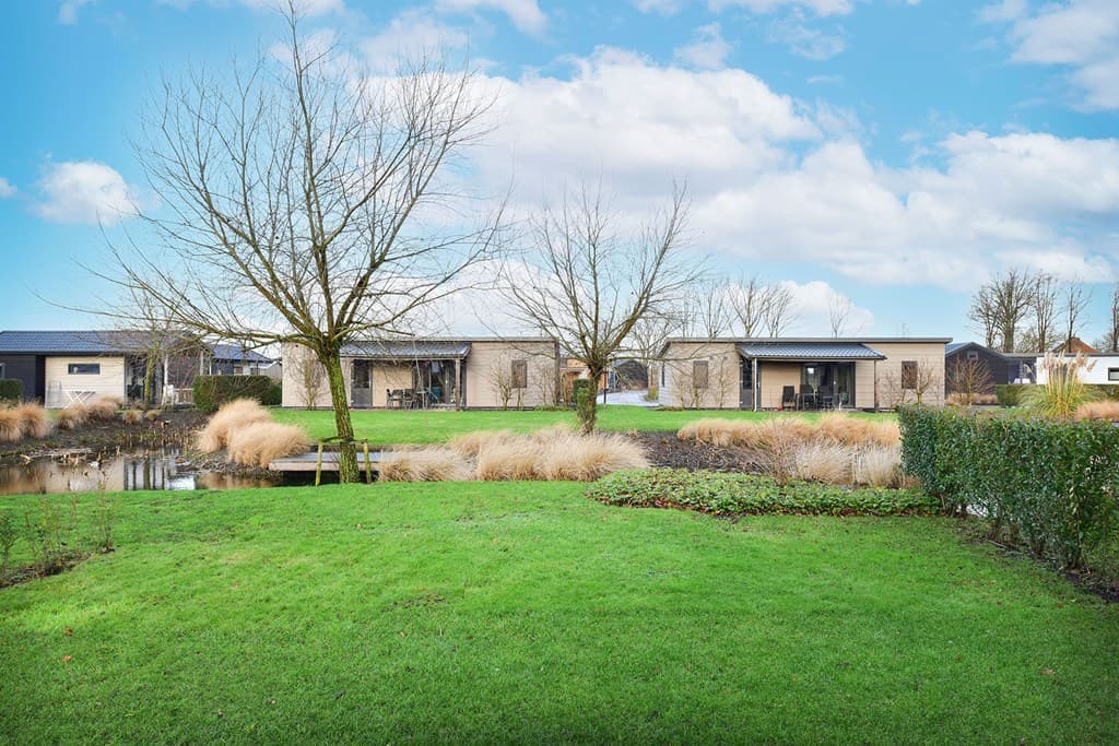 Drie vakantiewoningen aan een waterpartij omgeven door gras en bomen in Vakantiepark De Beemster, West-Graftdijk