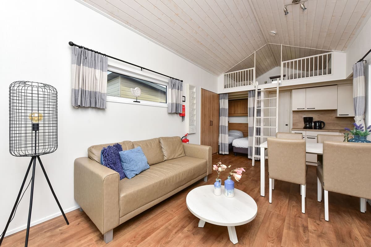 Woonruimte met een bank, tafel, kitchenette en bovenverdieping met een slaapgedeelte en ladder.